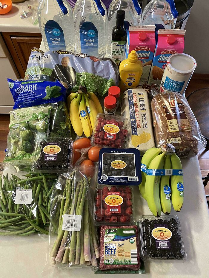 Grocery haul featuring fresh fruits, vegetables, eggs, oats, bread, and bottled water showing grocery costs where people live.