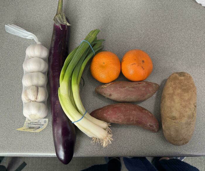 Garlic, eggplant, green onions, tangerines, sweet potatoes, and a large potato displayed as part of grocery cost comparison.