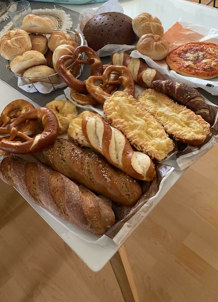 Assortment of freshly baked breads, pretzels, and pizza illustrating grocery cost variations where people live.