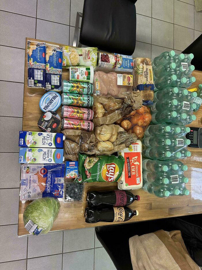 Groceries including water bottles, fresh produce, dairy, snacks, and beverages displayed on a table showing grocery costs.