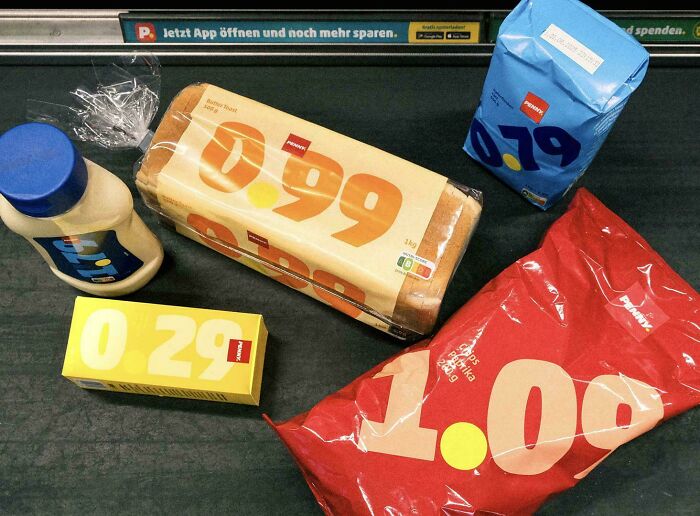 Groceries on a black surface showing prices on bread, milk, butter, sugar, and chips illustrating grocery cost differences.