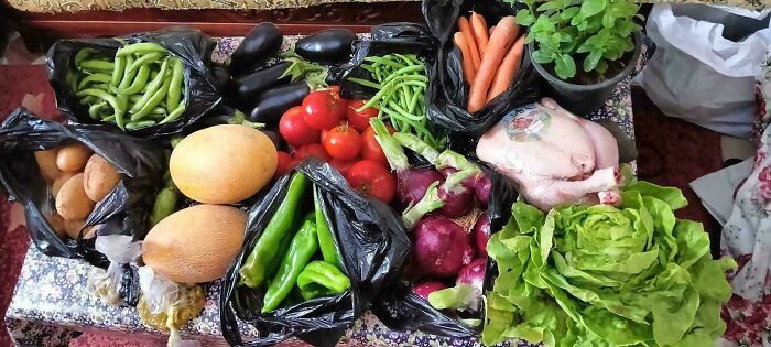 A variety of fresh groceries including vegetables, chicken, and herbs displayed on a table showing local grocery costs.