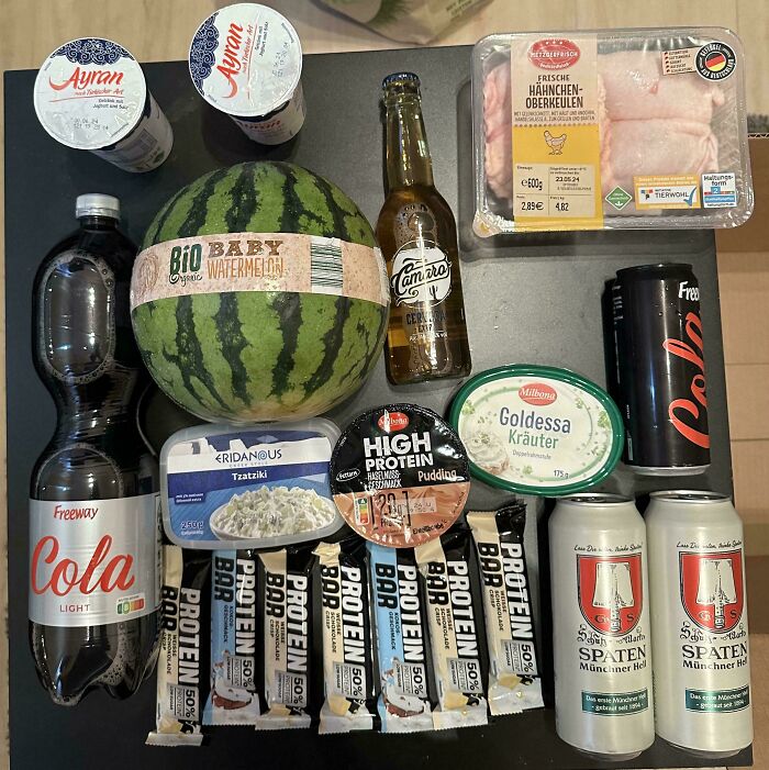 Groceries including watermelon, protein bars, chicken, drinks, and dairy products showing cost where they live.