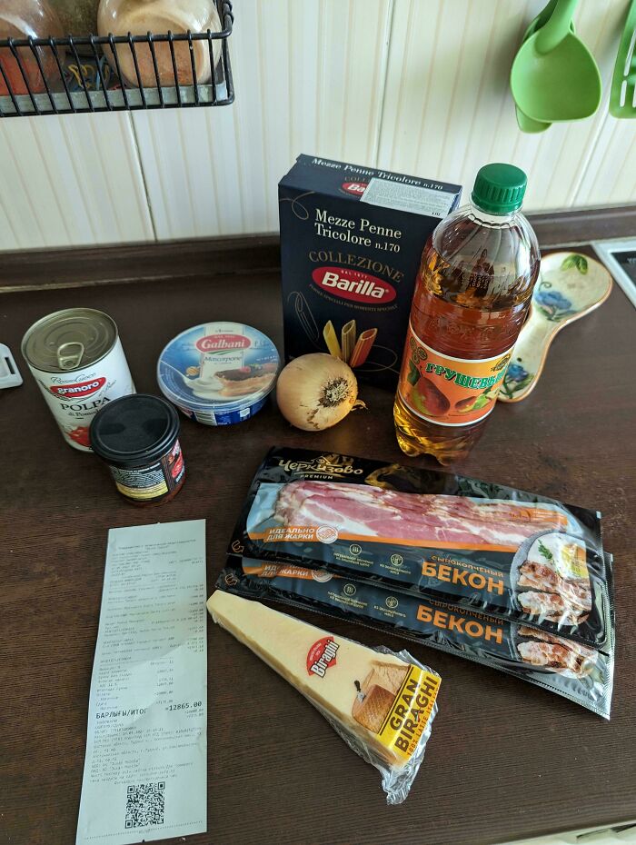 Groceries including pasta, cheese, bacon, onion, and tomato sauce displayed with a receipt showing grocery costs.