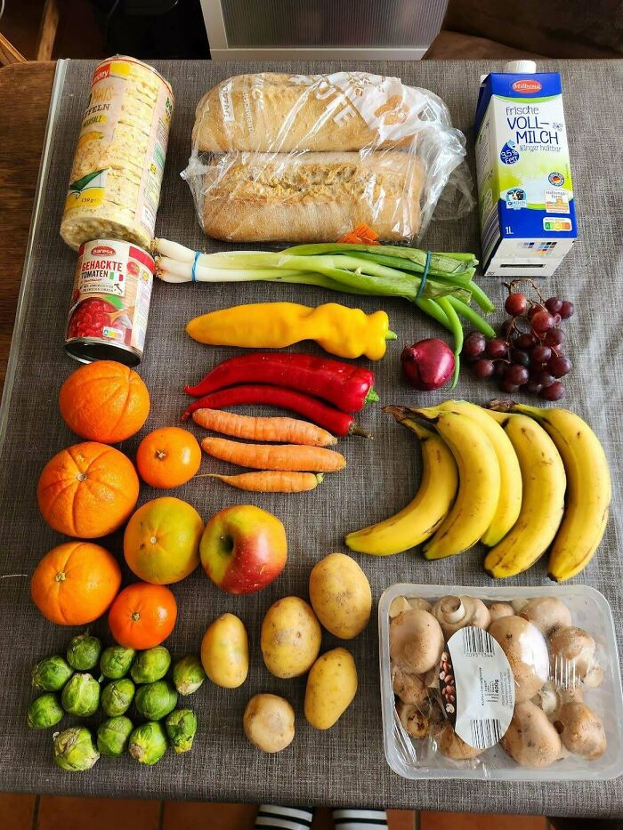 Various groceries including fruits, vegetables, bread, and milk displayed on a table showing grocery cost differences.