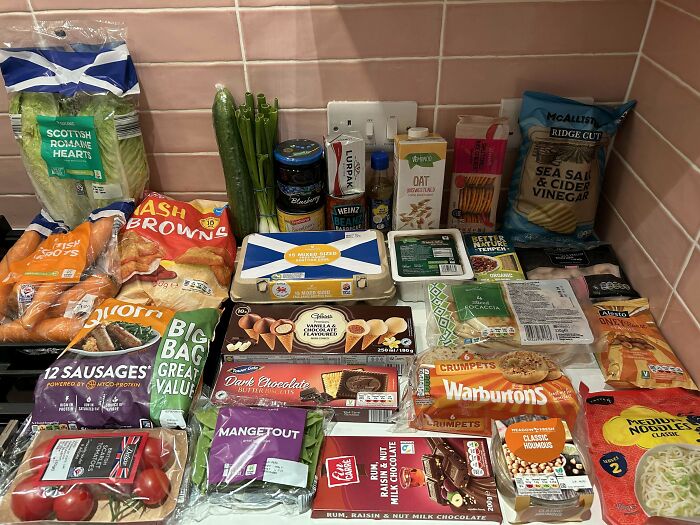 Groceries including vegetables, snacks, dairy, and packaged goods arranged on a kitchen counter showing typical grocery costs.