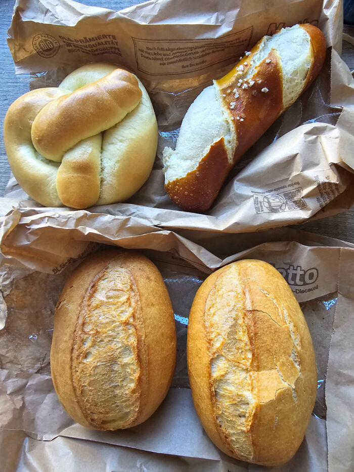 Various types of fresh bread on paper bags, illustrating grocery costs shared by 80 people where they live.
