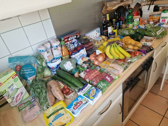 Groceries spread on a kitchen counter showing a variety of fresh produce and packaged foods depicting grocery costs.