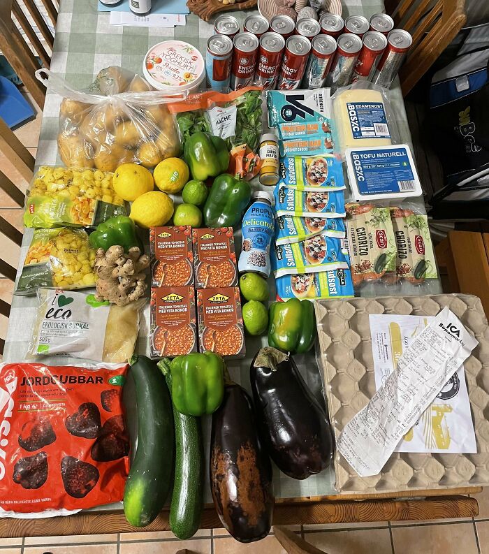 Groceries displayed on a table including vegetables, canned goods, drinks, and a receipt showing grocery costs where they live.