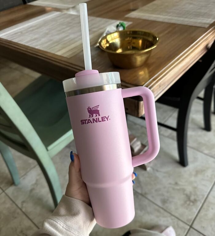 Pink Stanley tumbler with straw held over kitchen floor and wooden table, popular internet gold product found on Amazon.