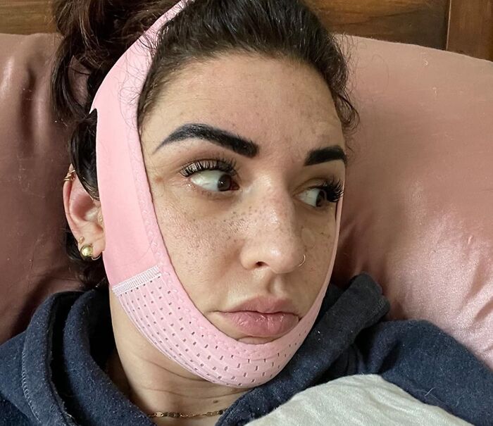 Woman wearing a pink face slimming strap lying on a pillow, demonstrating internet gold products found on Amazon.