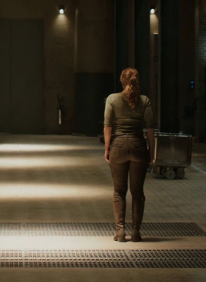 Woman standing alone in a dimly lit industrial space, a scene highlighting questionable movie details for cinephiles to mock.