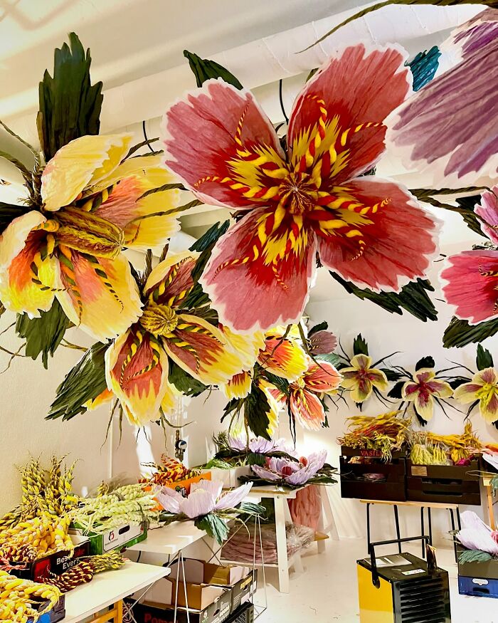 Giant tissue paper flowers in vibrant colors hanging and arranged in a bright creative studio workspace.
