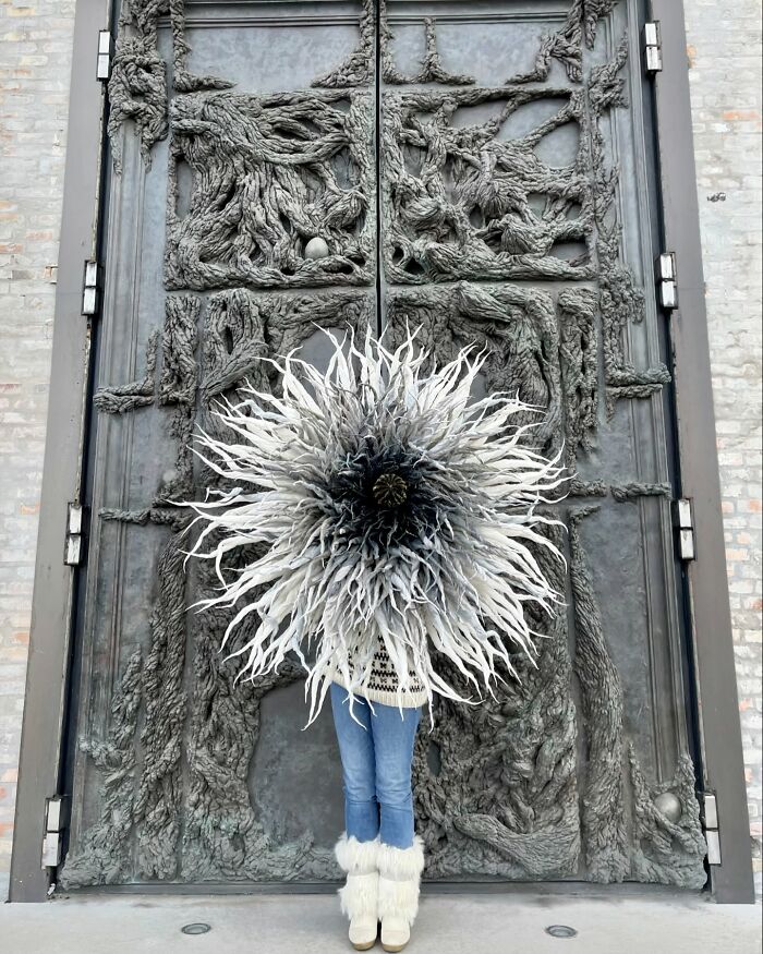 Woman holding a giant tissue paper flower with white and black petals standing in front of an intricate textured door.