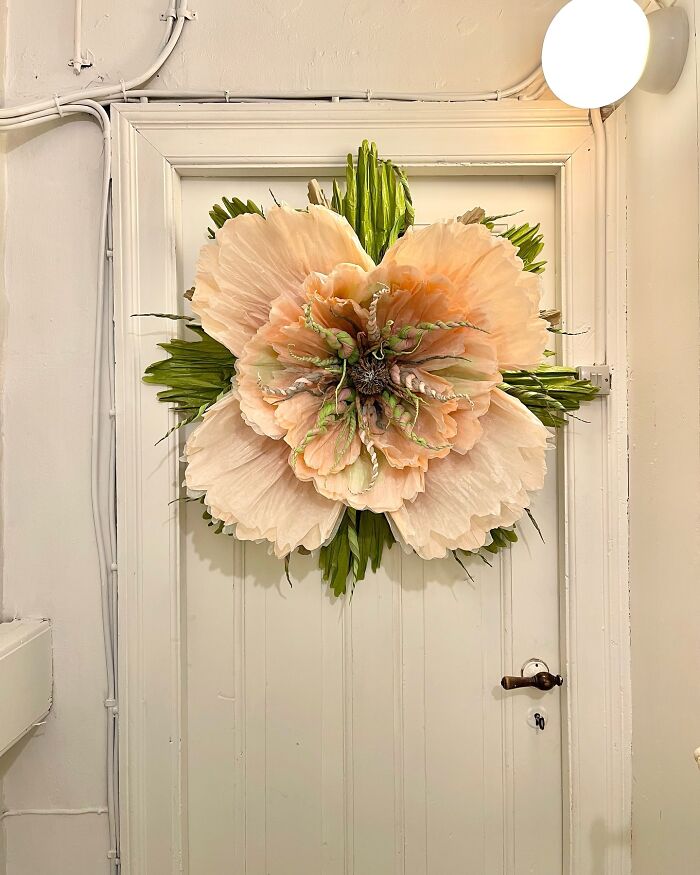Giant tissue paper flower with peach and green petals mounted on a white door in a cream-colored room.