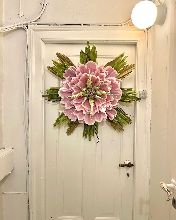 Giant pink and green tissue paper flower decoration hanging on a white door in a well-lit room.