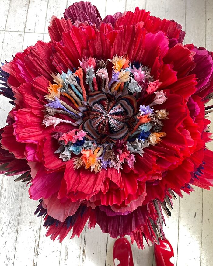 Giant tissue paper flower with vibrant red and multicolored petals displayed on a wooden floor.