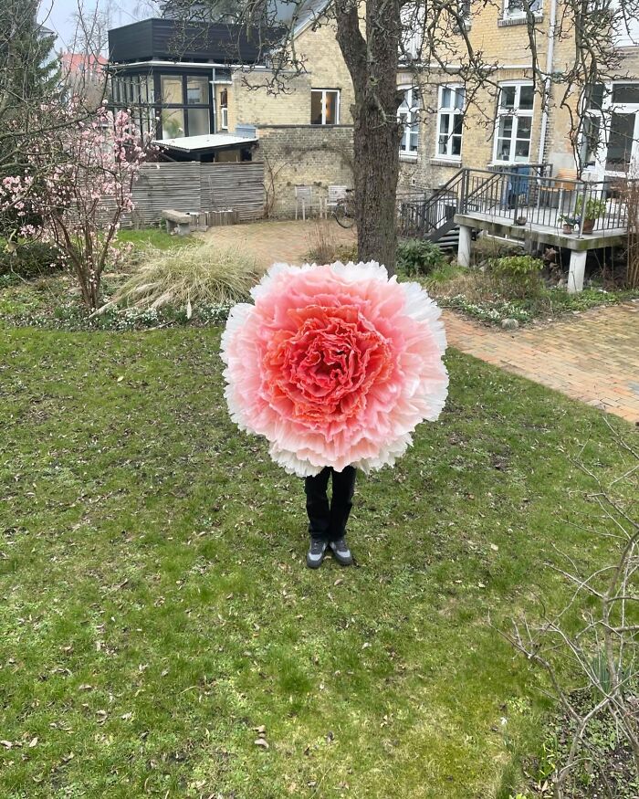 Person holding a giant tissue paper flower in a garden, showcasing creative large flower art made from tissue paper.