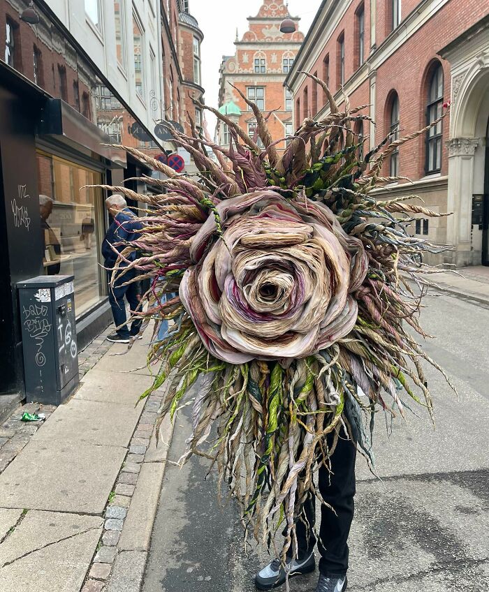 Person holding a giant tissue paper flower with twisted petals and leaves in an urban street setting.