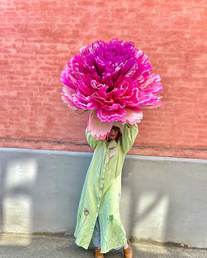 Woman holding a giant pink flower made of tissue paper, showcasing her creative giant flower artwork outdoors.