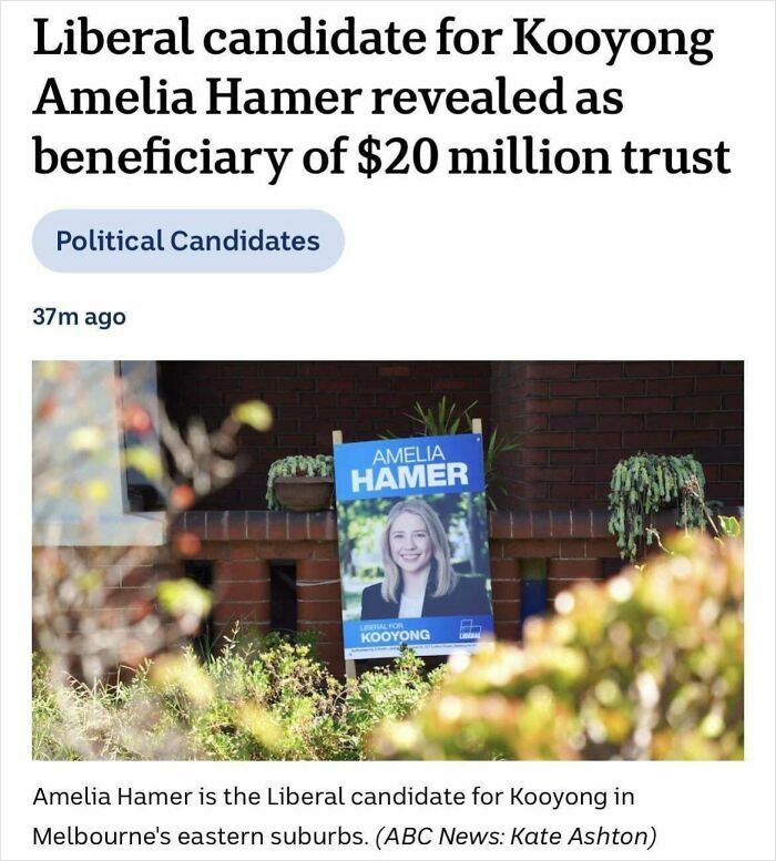 Political campaign poster of a Liberal candidate displayed outside a suburban home with surrounding plants and brick wall.