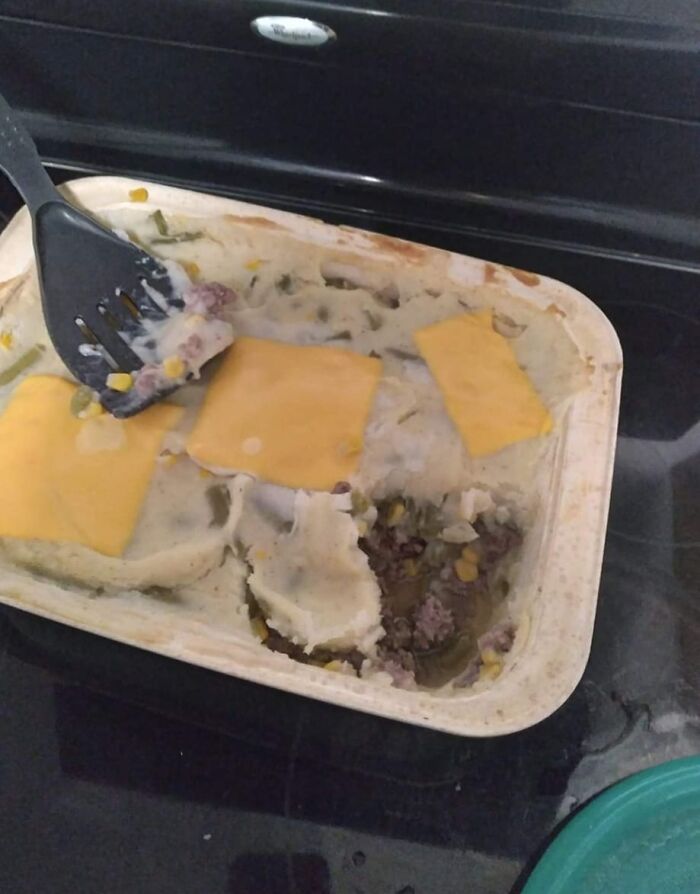 Cursed food pic of a poorly assembled shepherd's pie with slices of cheese on top in a baking dish.