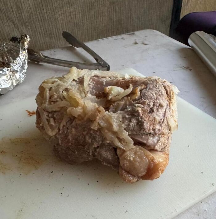 Unappetizing piece of cooked meat with onions on a cutting board, showing cursed food that looks unappealing