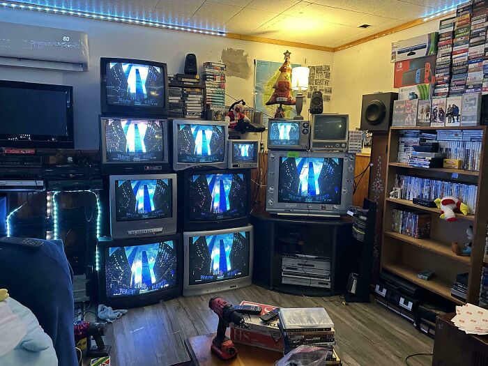 Multiple vintage CRT TVs stacked in a room surrounded by retro gaming devices and stacks of DVDs showcasing vintage devices.
