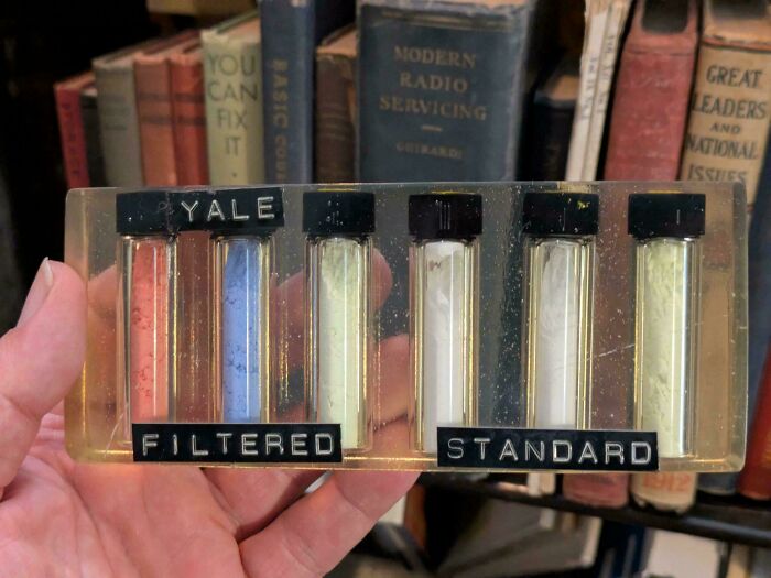 Hand holding vintage Yale glass test tubes with labeled filtered and standard powders, showcasing vintage devices technology.
