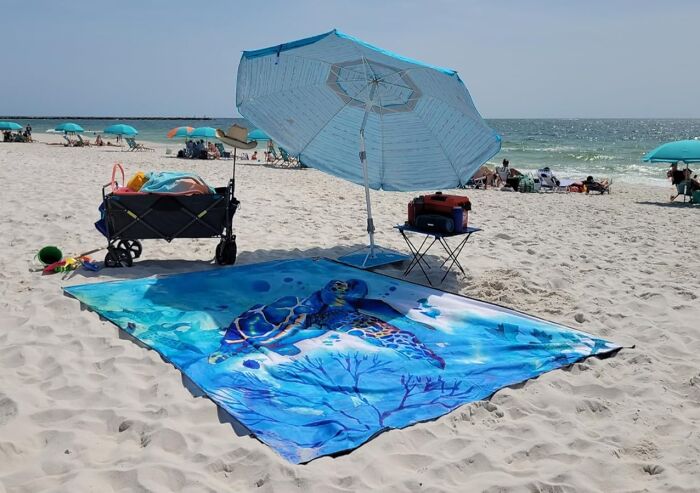 Beach setup with umbrella, turtle print beach towel, and summer essentials for viral summer essentials on white sand.