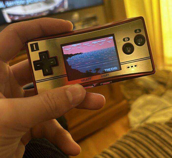 Hand holding a vintage handheld gaming device showing a pixelated game screen, highlighting vintage devices technology.