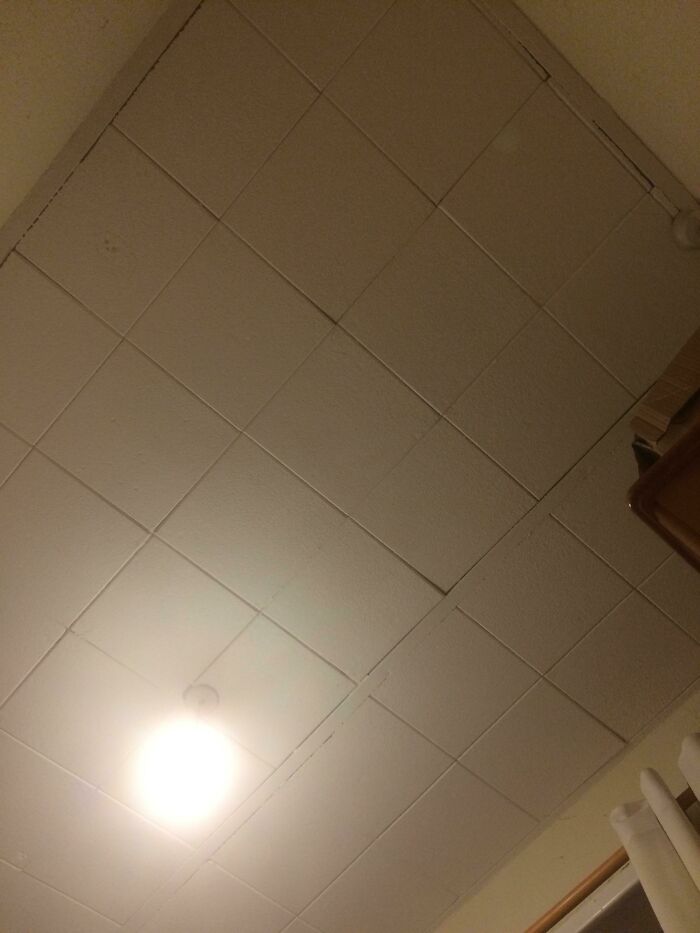 Worn ceiling tiles with uneven gaps and a bright light bulb, showcasing infuriating landlord specials in rental housing.