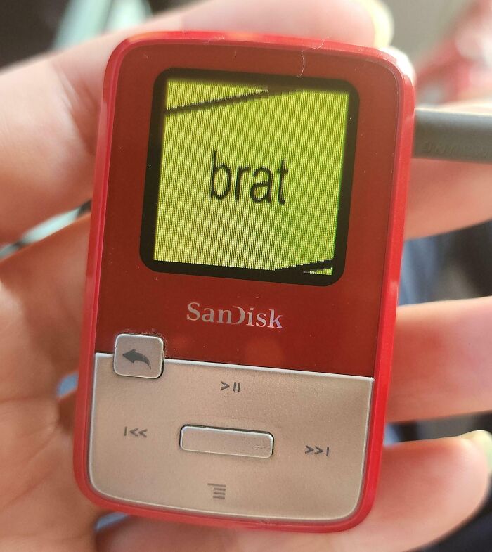 Hand holding a vintage SanDisk MP3 player with a yellow screen displaying text, showcasing vintage devices and technology evolution.