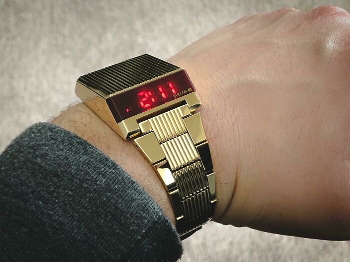 Vintage digital wristwatch with red LED display on a gold metal band showcasing retro technology devices.