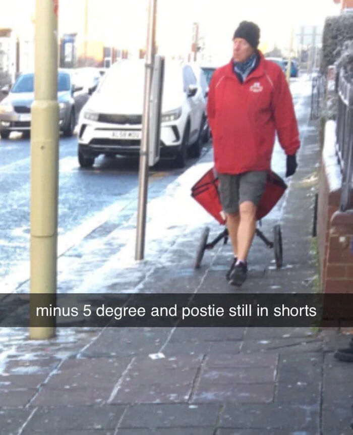 Postman wearing shorts and a jacket delivering mail on a snowy sidewalk in a typical Great British memes moment.