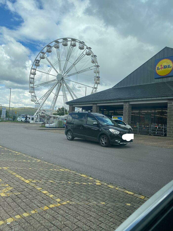 Ferris wheel near a Lidl store parking lot on a cloudy day, capturing a scene of everyday Great British memes.