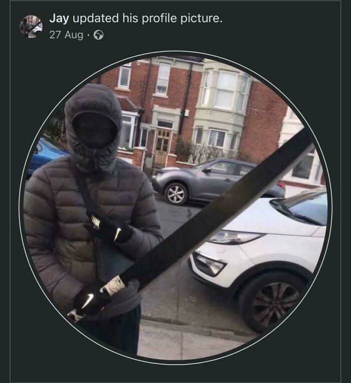 Person in dark puffer jacket and hood holding an oversized machete on a residential street in a Great British meme.