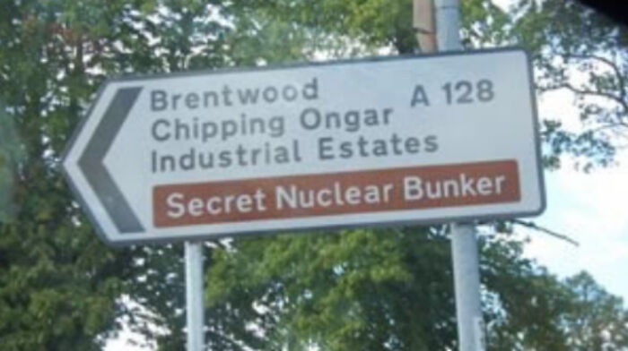 Road sign in the UK pointing to Brentwood and Chipping Ongar with directions to a secret nuclear bunker, British meme humor.