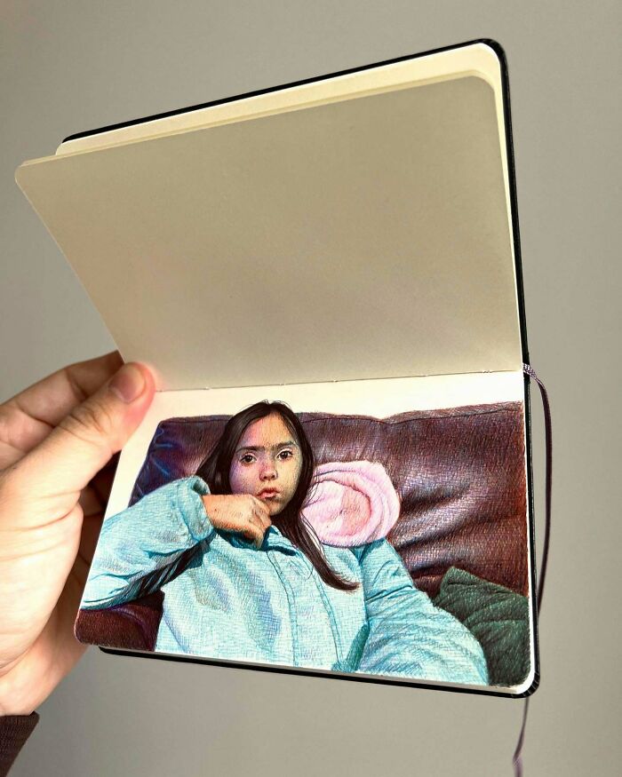 Hand holding tiny sketchbook with detailed colored drawing of a thoughtful girl on a couch, capturing big emotions.