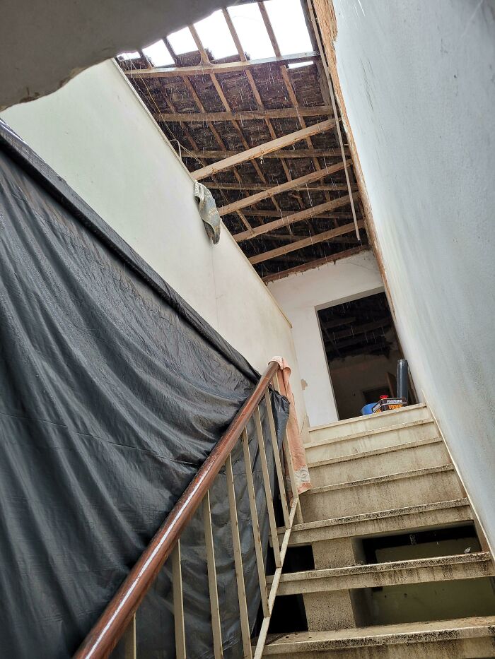 Staircase with missing roof panels causing rain to pour inside, showing a failed renovation saving attempt.