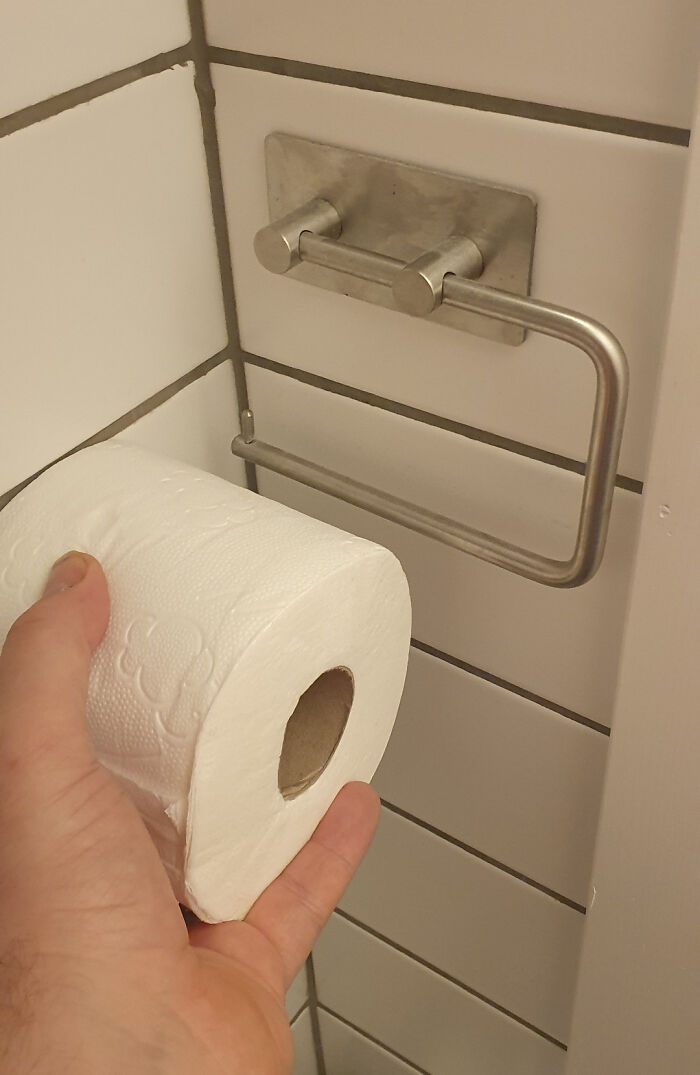Hand holding a toilet paper roll in front of an unusable holder, a funny renovation fail saving on renovations.