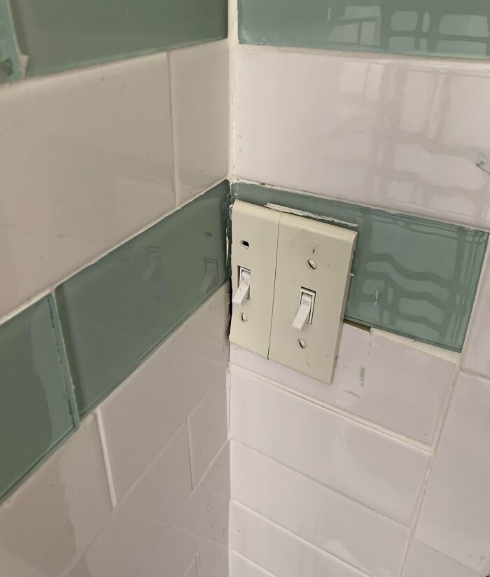 Light switch poorly installed among bathroom tiles, illustrating a funny renovation fail with saving attempts.
