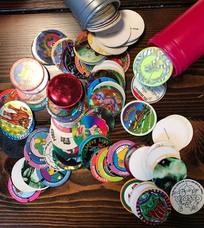 Colorful vintage pogs and slammers spilled from cans, showcasing nostalgic cringey nineties fashion collectibles.