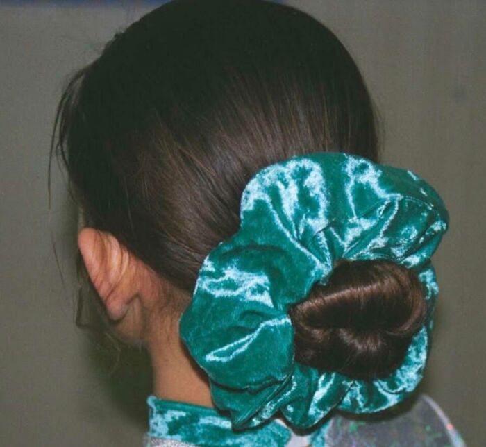 Woman with dark hair styled in a bun secured by a large green velvet scrunchie, a popular nineties fashion accessory.