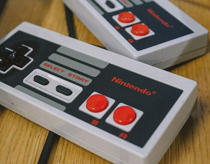 Retro Nintendo game controllers with red buttons on a wooden surface, symbolizing dark family secrets shared in adulthood.