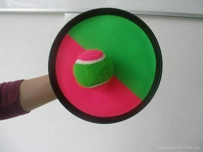 Hand holding a colorful plastic catch ball paddle with a green and pink fuzzy ball, a nostalgic nineties fashion accessory.