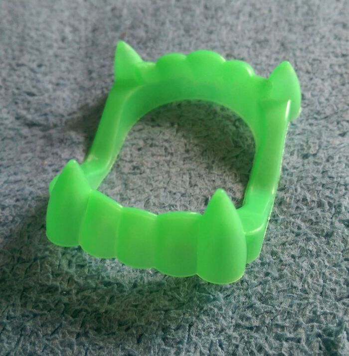 Green plastic vampire teeth toy representing cringey nineties fashion accessory left behind from the decade.