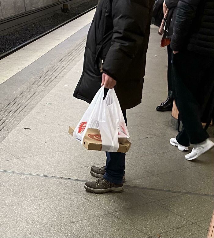 Person at a train station holding pizza boxes with plastic bags as an inventive way to carry food items.