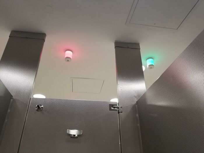 Bathroom stall with red and green lights above doors indicating occupancy, an ingenious solution for overlooked issues.