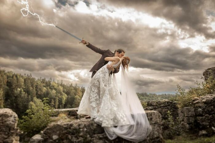 Couple in wedding attire posing on rocks with groom holding a lightning sword, showcasing humorous Photoshop skills outdoors.